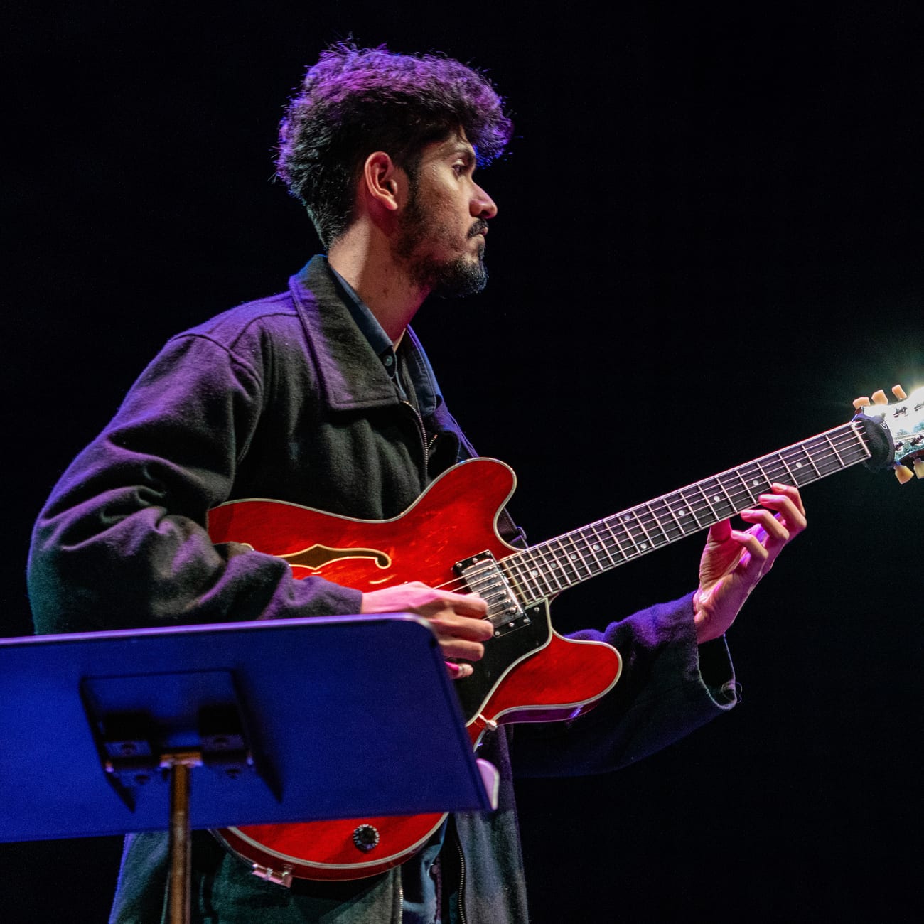 Varad Sahasrabudhe playing his red archtop guitar on stage